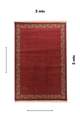 Alfombra rectangular de 2 x 3 metros con fondo rojo, patrón repetitivo de inspiración oriental, bordes ornamentales detallados y flecos claros en ambos extremos.