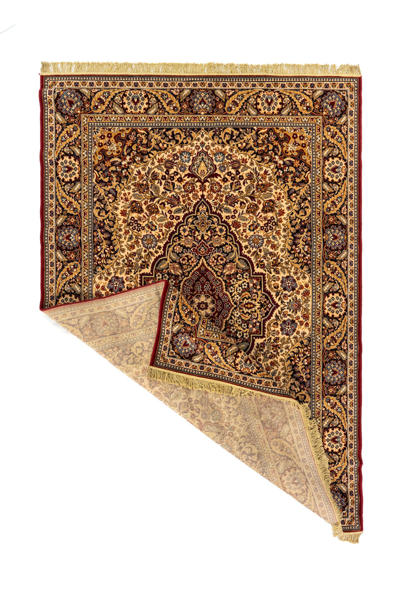 Alfombra clásica rectangular con una esquina doblada que muestra el reverso del tejido, los flecos y el detalle del diseño decorativo
