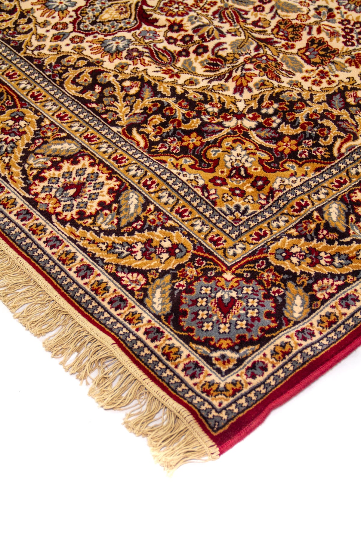 Detalle de esquina de alfombra oriental con fondo beige, borde floral en azul y dorado, y flecos claros en el extremo