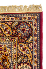 Detalle lateral de alfombra oriental con flecos beige y borde floral tradicional en tonos azul oscuro, dorado y rojo oscuro