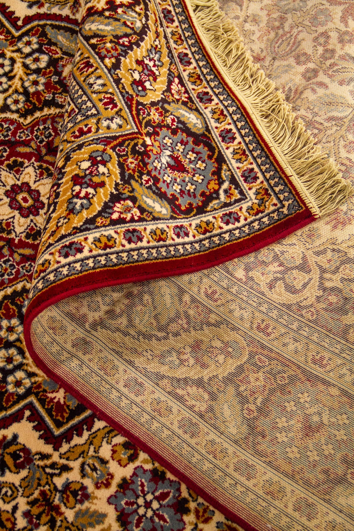 Detalle de alfombra doblada mostrando la textura, el reverso del tejido y el diseño floral ornamental del borde