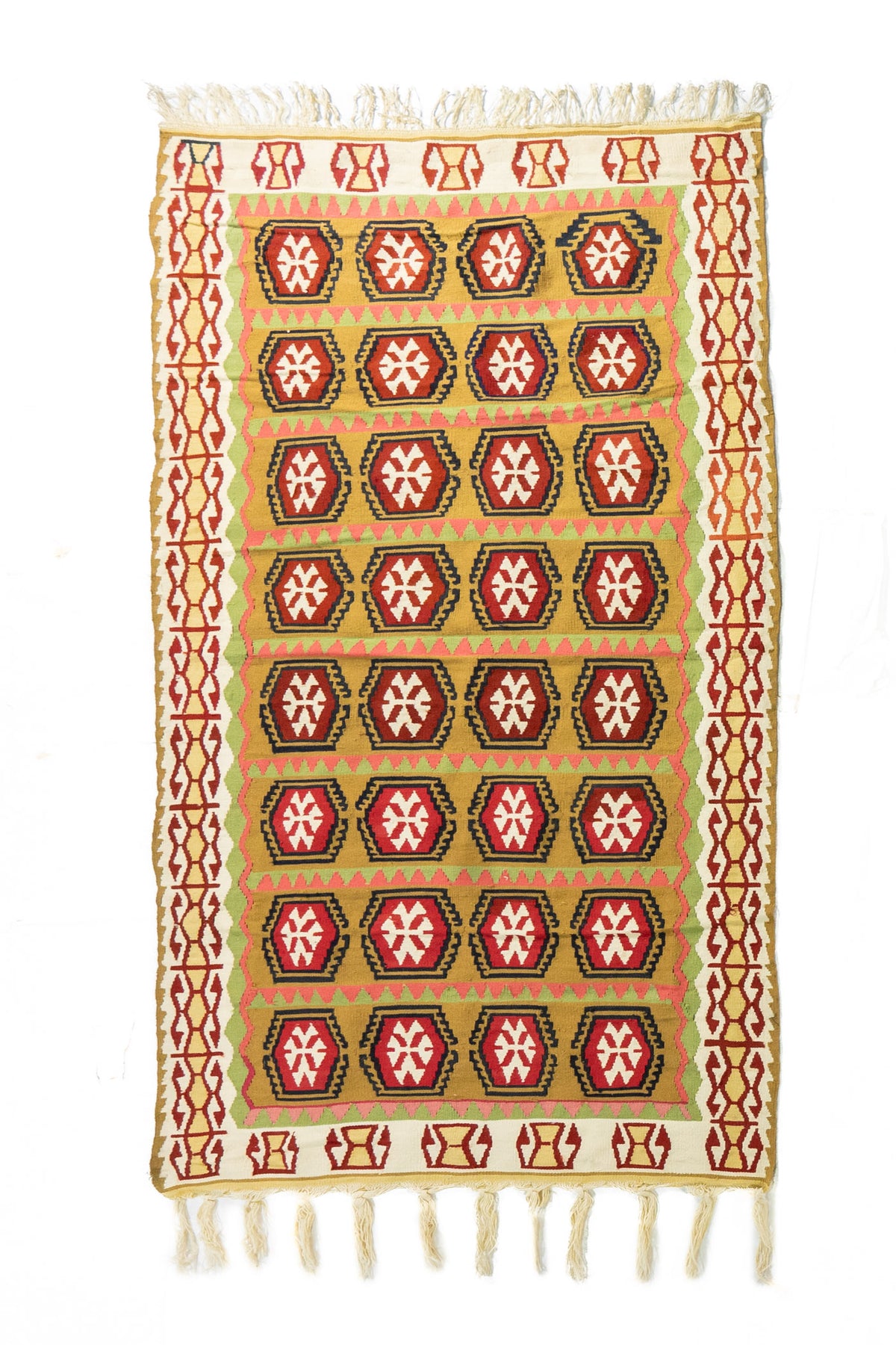 Alfombra rectangular artesanal en tonos beige, dorado, rojo y verde, con diseño geométrico repetitivo y flecos en ambos extremos.