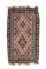 Alfombra rectangular artesanal en tonos rosa cálido, azul, marrón y negro, con diseño geométrico simétrico y flecos en ambos extremos.