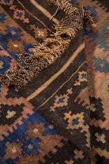 Detalle de alfombra doblada que muestra el reverso, los flecos y los patrones geométricos en tonos azul, marrón, rosa cálido y negro.