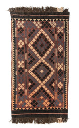 Alfombra rectangular artesanal en tonos marrón, negro, beige y gris, con diseño geométrico tribal de rombos entrelazados y flecos en ambos extremos.