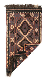 Alfombra geométrica tejida con una esquina doblada, en colores marrón oscuro, negro, beige y azul oscuro, que muestra su flexibilidad y acabado artesanal.