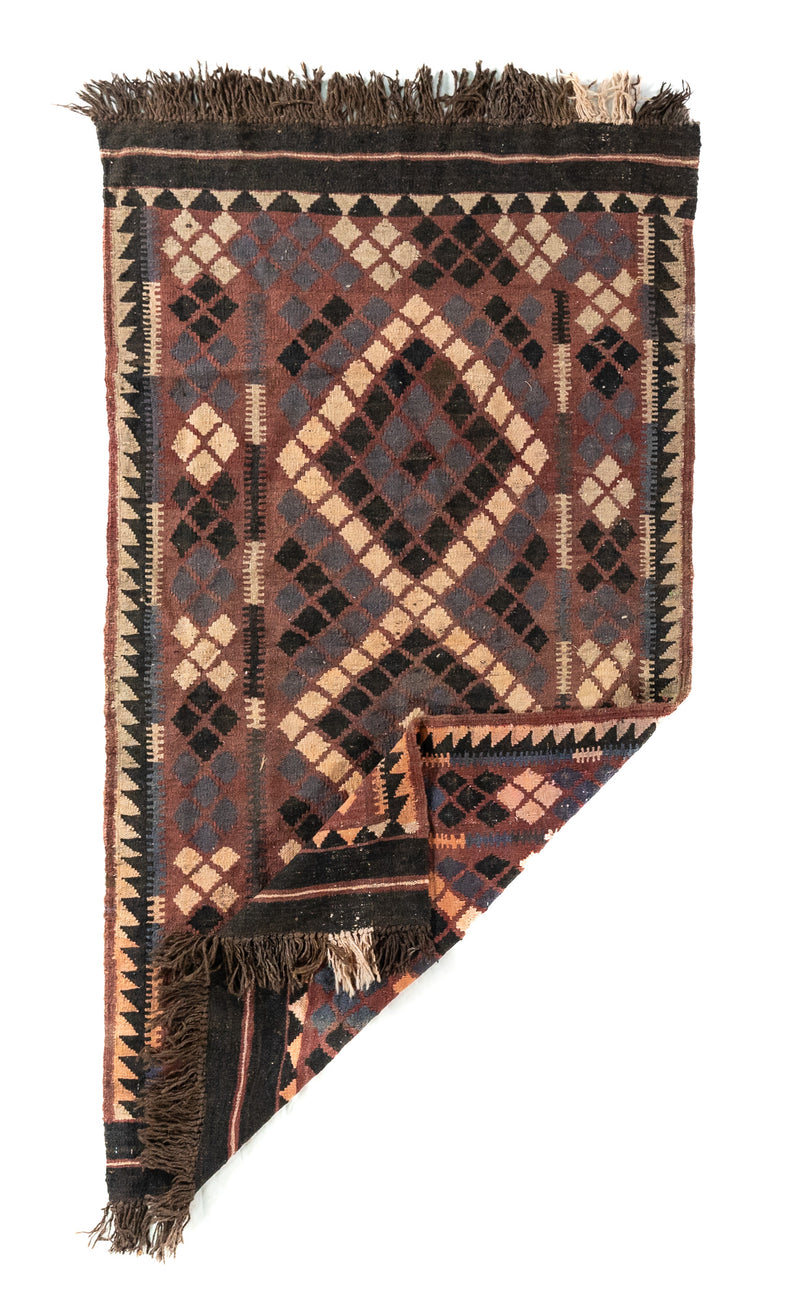 Alfombra geométrica tejida con una esquina doblada, en colores marrón oscuro, negro, beige y azul oscuro, que muestra su flexibilidad y acabado artesanal.