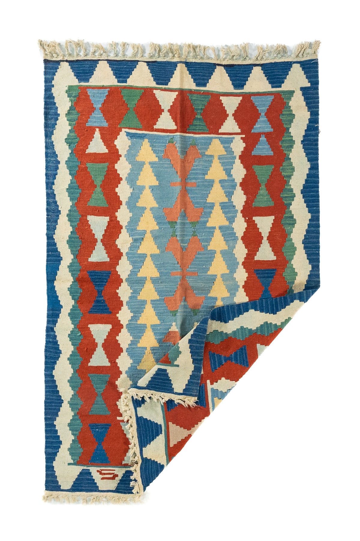 Alfombra kilim doblada en una esquina, mostrando su reverso, flexibilidad y tejido artesanal de trama plana.