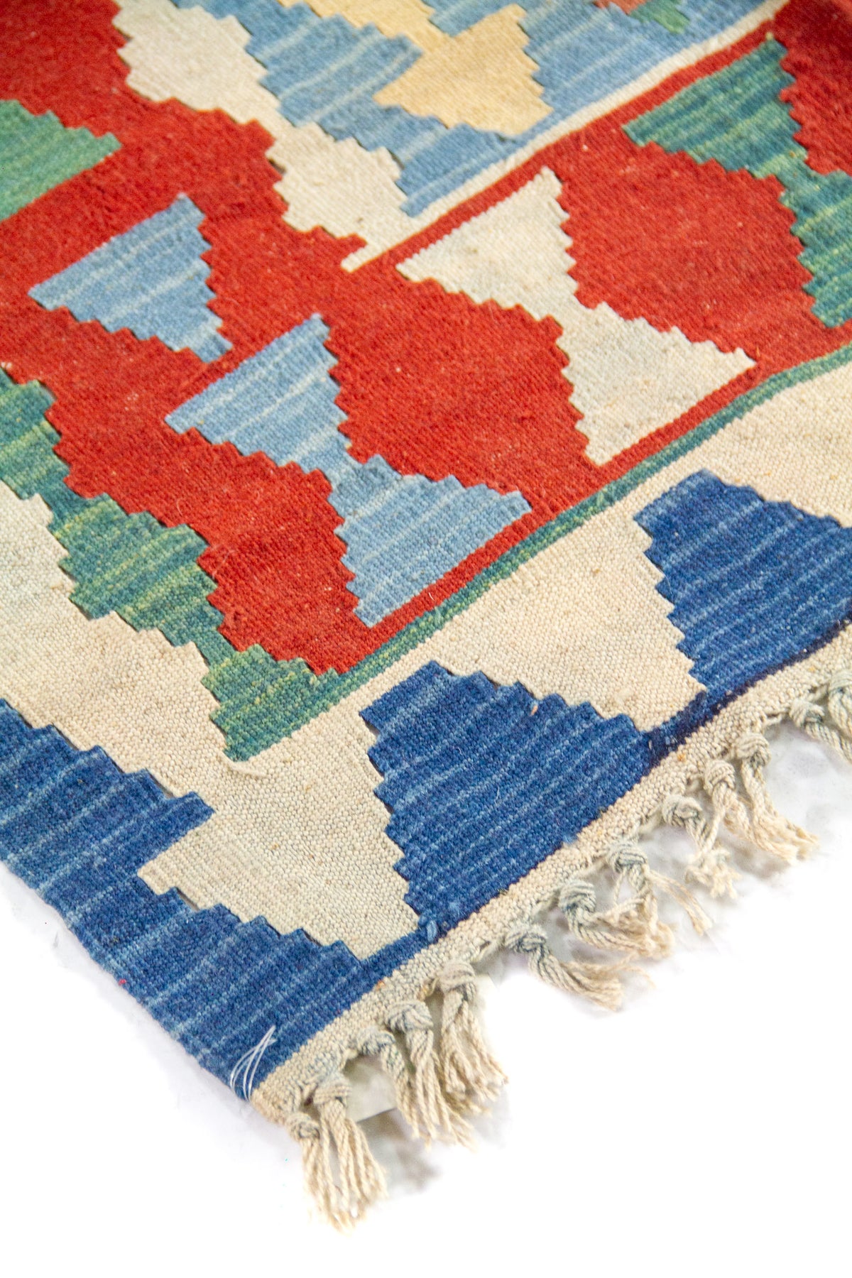 Primer plano de borde con flecos de una alfombra kilim en tonos azul, rojo, beige y verde suave.