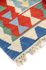 Primer plano de borde con flecos de una alfombra kilim en tonos azul, rojo, beige y verde suave.