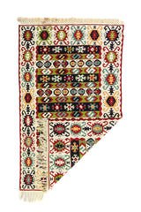 Alfombra geométrica artesanal con una esquina doblada, en colores, blanco, rojo, verde y negro, que muestra su textura y flexibilidad.