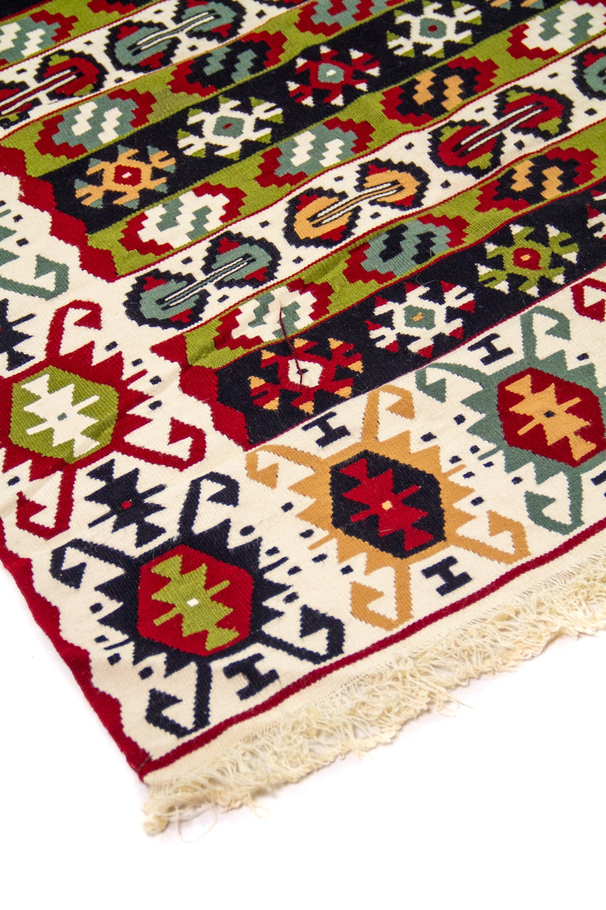 Detalle de esquina de alfombra tipo kilim con franjas geométricas multicolor, borde blanco y flecos tejidos en tono natural.