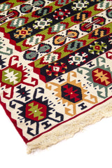 Detalle de esquina de alfombra tipo kilim con franjas geométricas multicolor, borde blanco y flecos tejidos en tono natural.