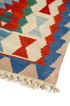 Acercamiento al diseño lateral de alfombra artesanal con motivos geométricos repetitivos en azul, rojo y beige, y textura de tejido visible.