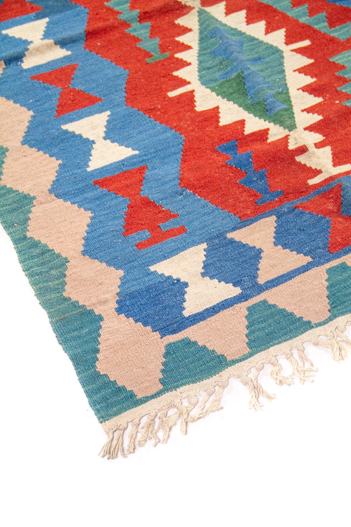 Detalle de esquina de alfombra kilim con flecos y patrones geométricos en azul, rojo y beige.
