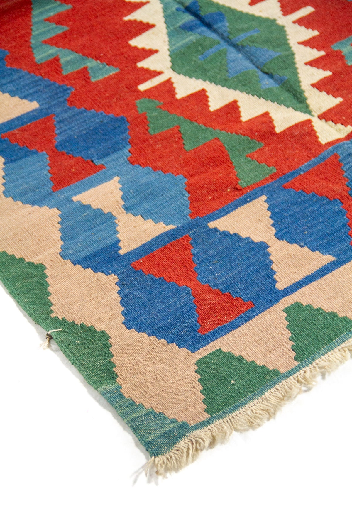 Detalle de alfombra artesanal con motivos geométricos escalonados en rojo, azul, verde y beige.