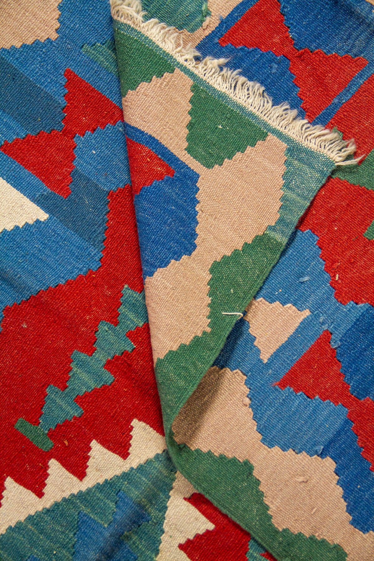 Detalle de alfombra doblada que muestra la textura del tejido y sus figuras geométricas multicolor.
