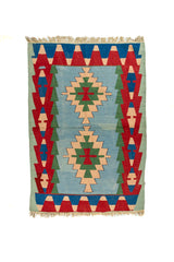Alfombra estilo kilim con diseño geométrico en tonos celeste, rojo, azul, verde y beige.