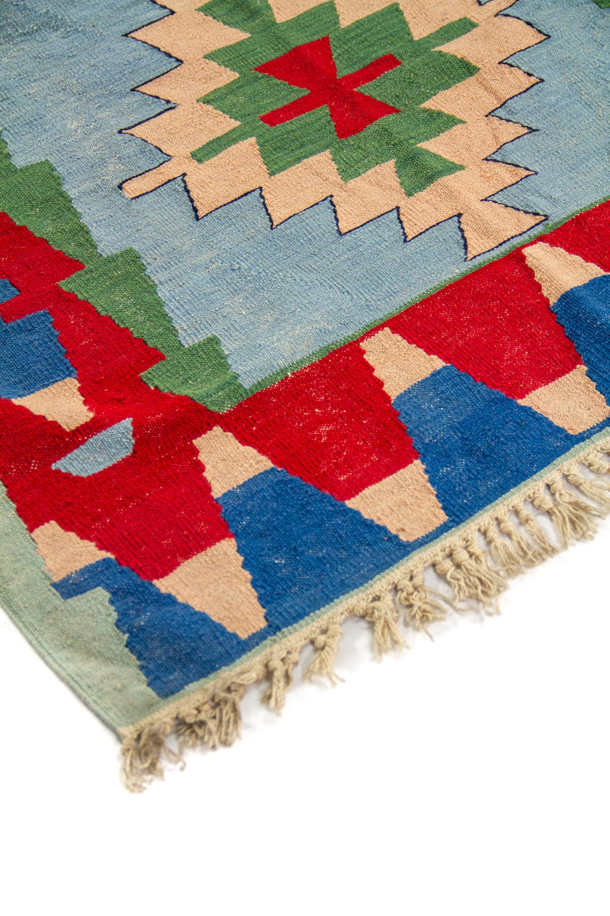 Detalle de alfombra artesanal con medallón geométrico central sobre fondo celeste y borde decorativo multicolor.