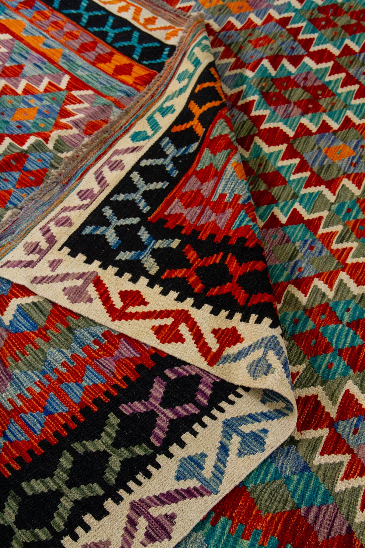 Detalle de pliegue de alfombra Kilim con guarda negra y diseño geométrico multicolor