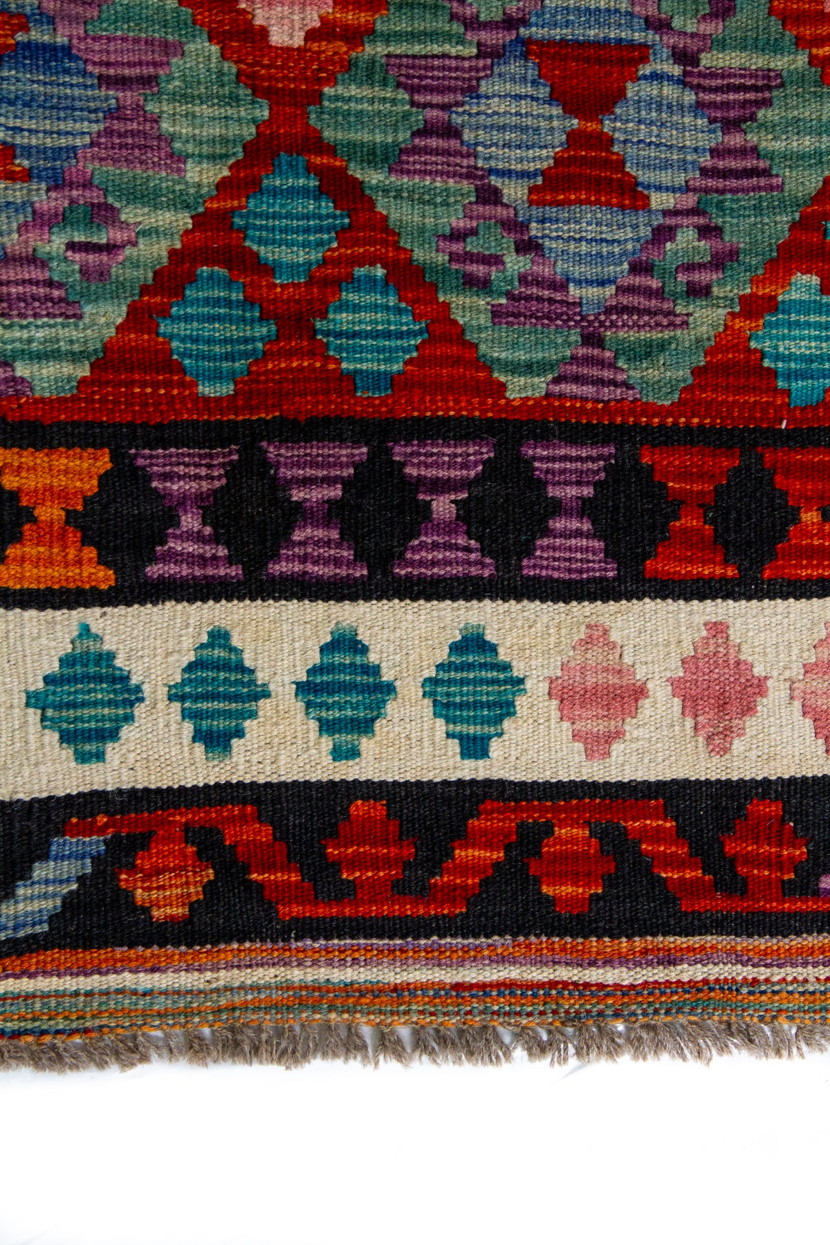 Detalle de guarda y flecos de alfombra Kilim multicolor con motivos geométricos