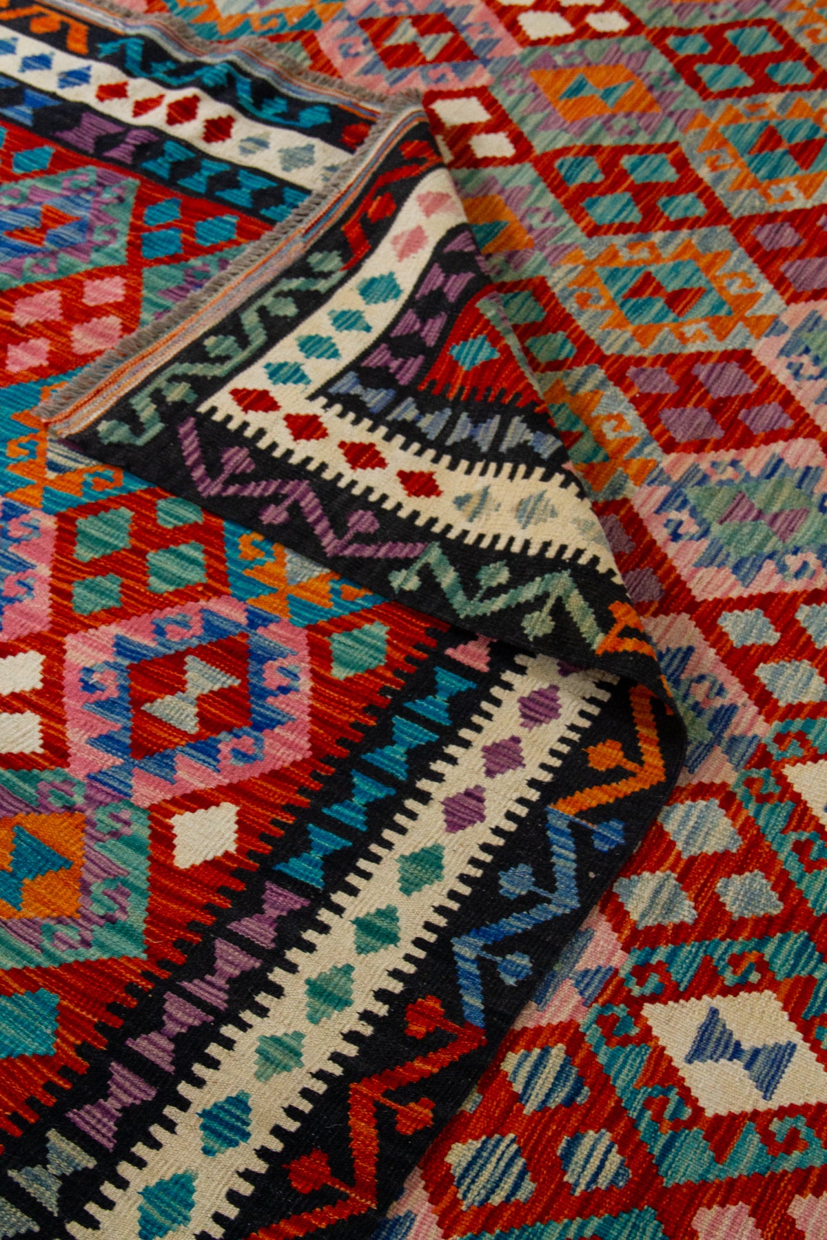 Detalle de pliegue de alfombra Kilim con guarda negra y diseño geométrico multicolor
