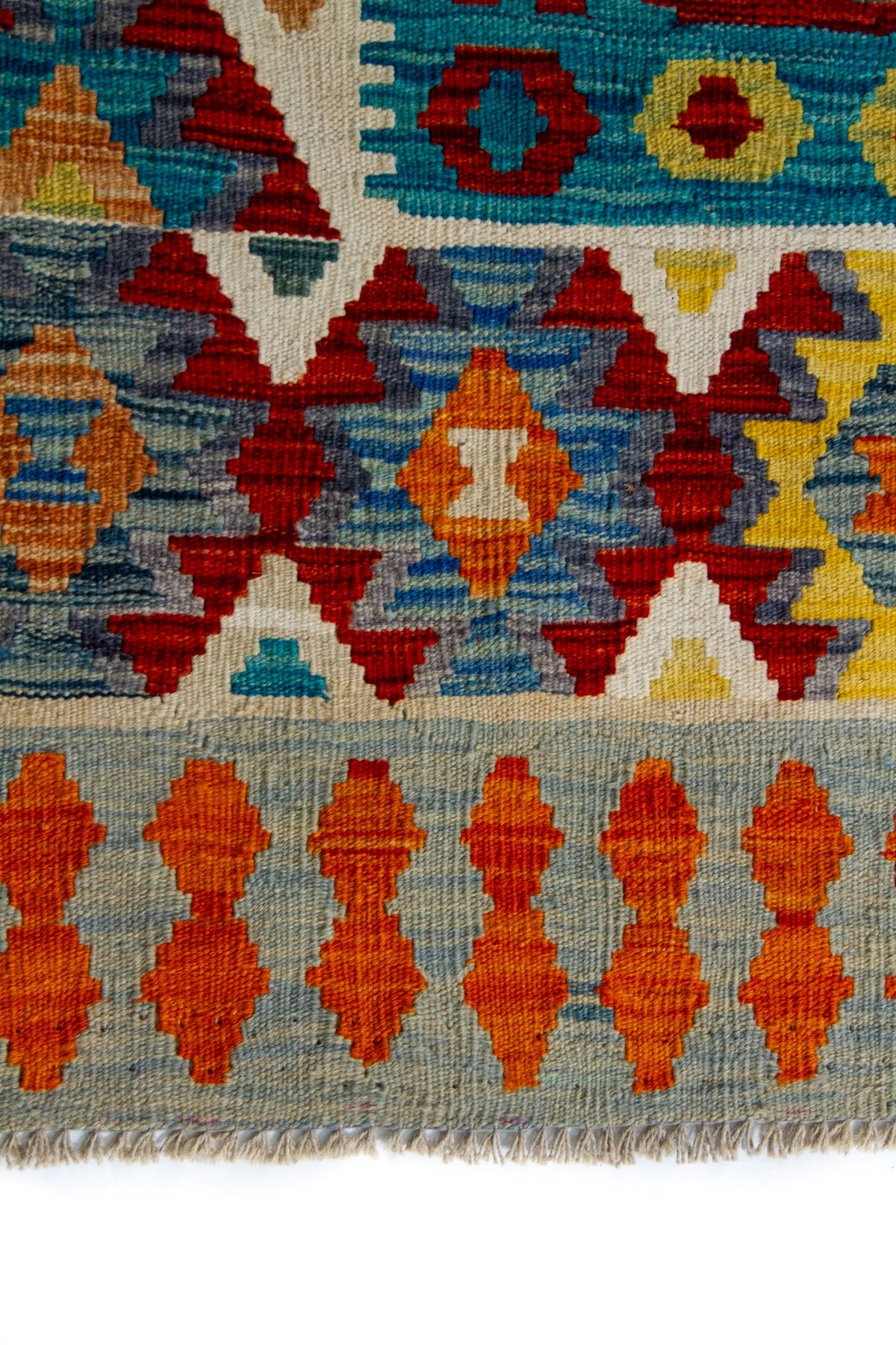 Detalle de guarda y flecos de alfombra Kilim multicolor con motivos geométricos en naranja, rojo y azul