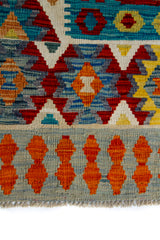 Detalle de guarda y flecos de alfombra Kilim multicolor con motivos geométricos en naranja, rojo y azul