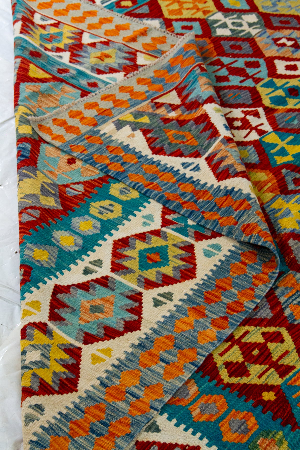 Detalle del borde doblado de alfombra Kilim multicolor con guardas geométricas y textura visible