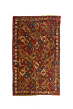 Alfombra artesanal rectangular en tonos rojo, beige, azul y marrón con diseño geométrico repetitivo y guarda decorativa clara