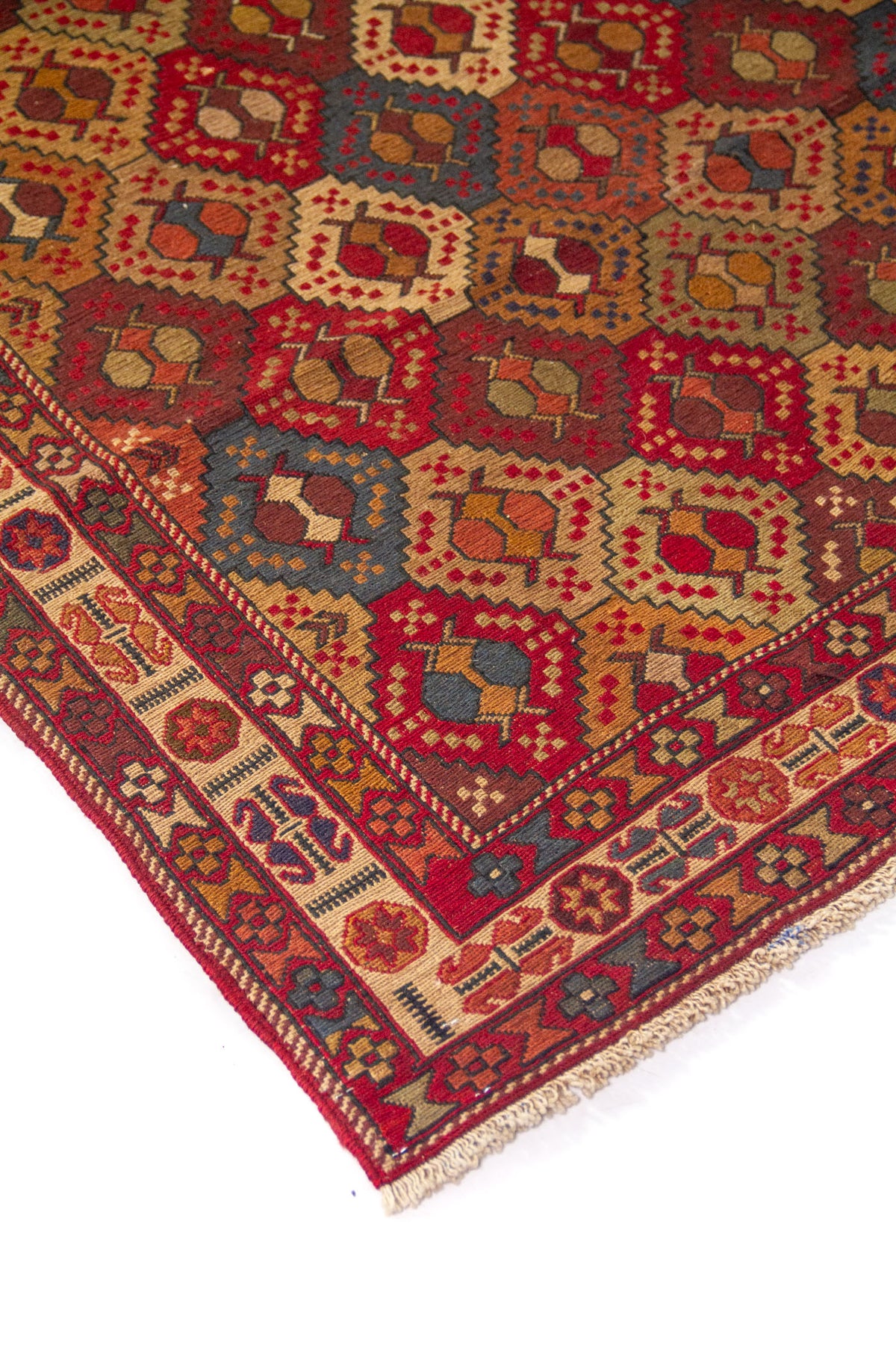 Detalle de esquina de alfombra vintage con motivos geométricos en forma de rombos y guarda ornamental en tonos rojos, beige y azul