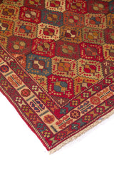 Detalle de esquina de alfombra vintage con motivos geométricos en forma de rombos y guarda ornamental en tonos rojos, beige y azul