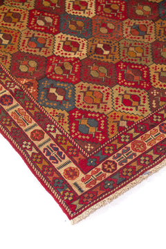 Detalle de esquina de alfombra vintage con motivos geométricos en forma de rombos y guarda ornamental en tonos rojos, beige y azul