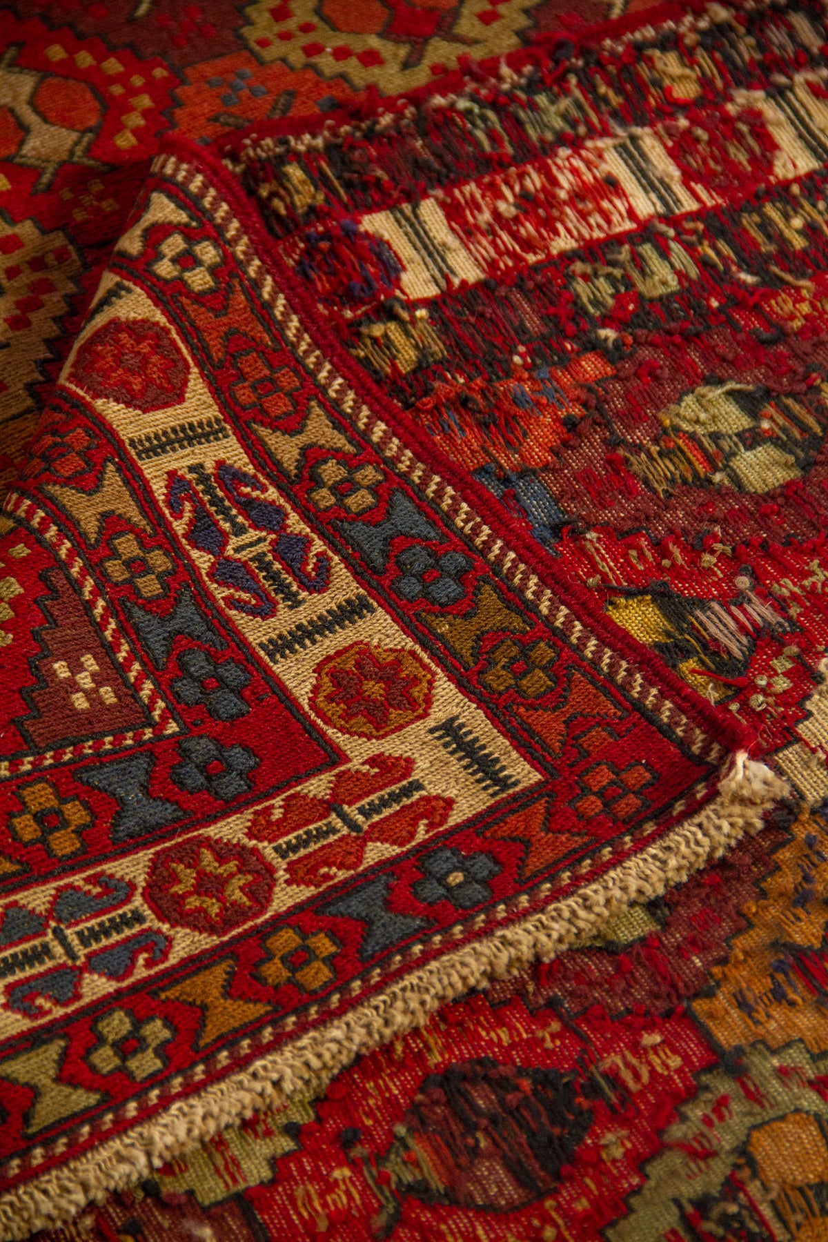Detalle de alfombra doblada que muestra la textura del tejido, la guarda decorativa y el reverso de la pieza