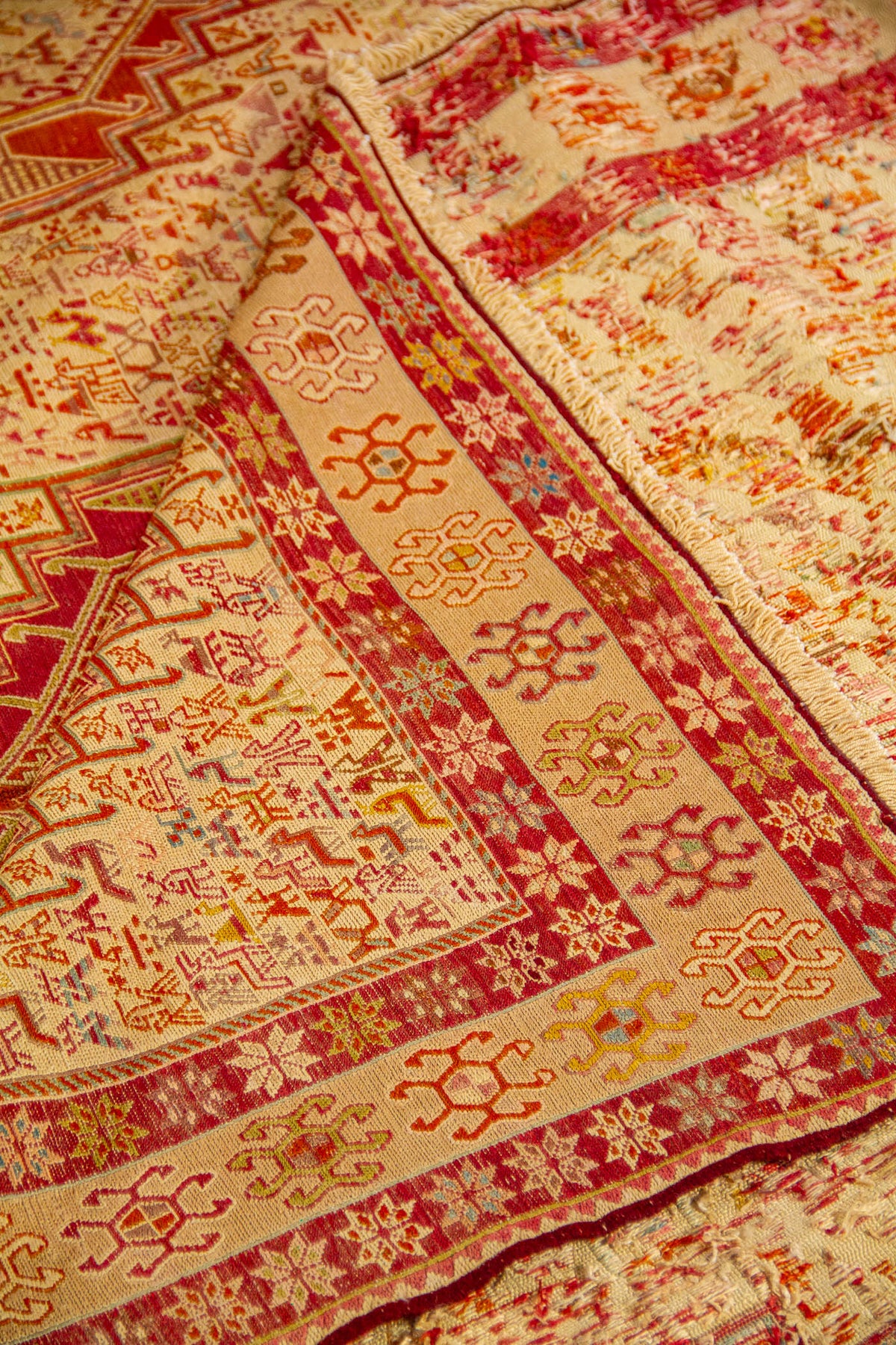 Detalle de alfombra doblada mostrando la textura tejida y los diseños geométricos en tonos rojo y beige