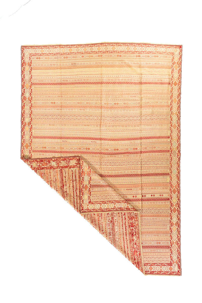 Alfombra tejida en tonos cálidos con una esquina doblada que muestra el reverso y su diseño lineal