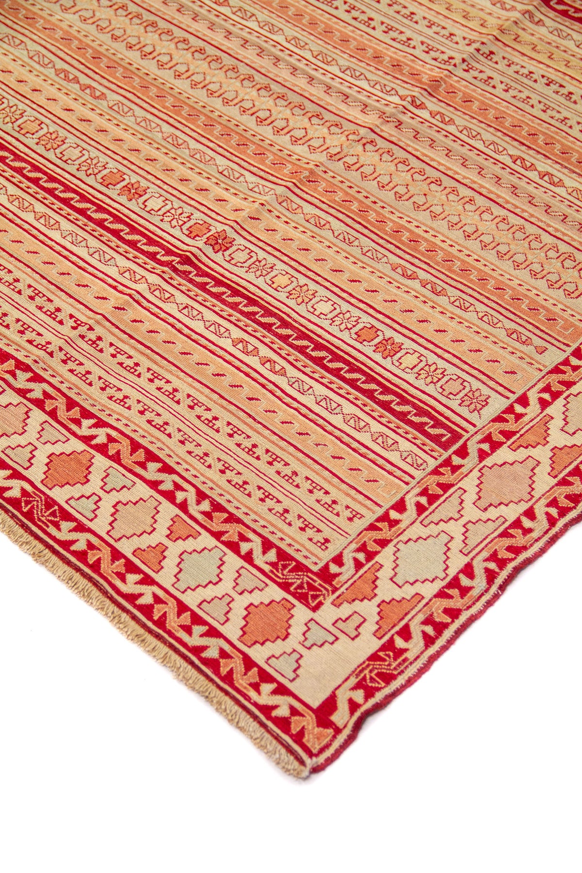 Detalle de esquina de alfombra con franjas decorativas en rojo, beige y anaranjado suave y borde geométrico
