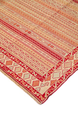 Detalle de esquina de alfombra con franjas decorativas en rojo, beige y anaranjado suave y borde geométrico