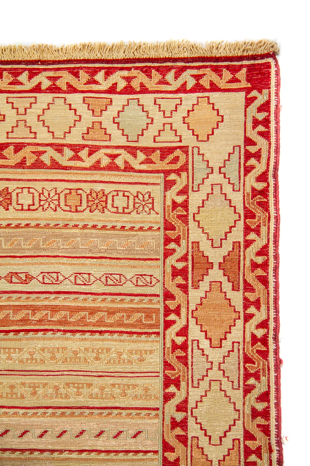 Detalle del borde de alfombra con motivos geométricos escalonados en beige y rojo 