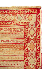 Detalle del borde de alfombra con motivos geométricos escalonados en beige y rojo 