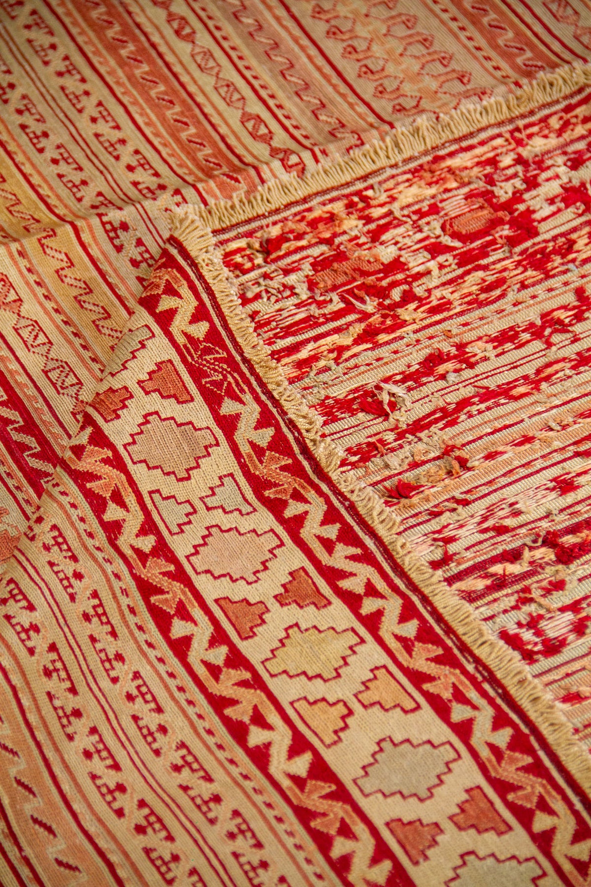 Detalle de alfombra doblada mostrando la textura tejida, el reverso y su patrón lineal tradicional