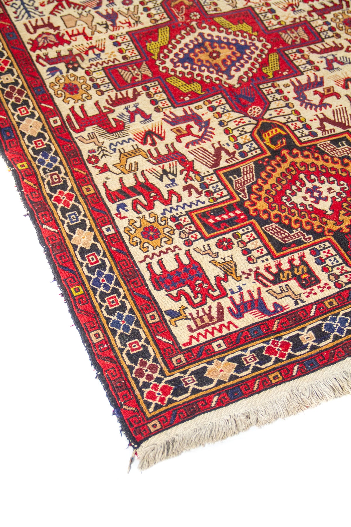 Detalle de esquina de alfombra artesanal con guarda geométrica en rojo y azul, fondo blanco y flecos en beige