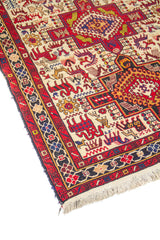 Detalle de esquina de alfombra artesanal con guarda geométrica en rojo y azul, fondo blanco y flecos en beige