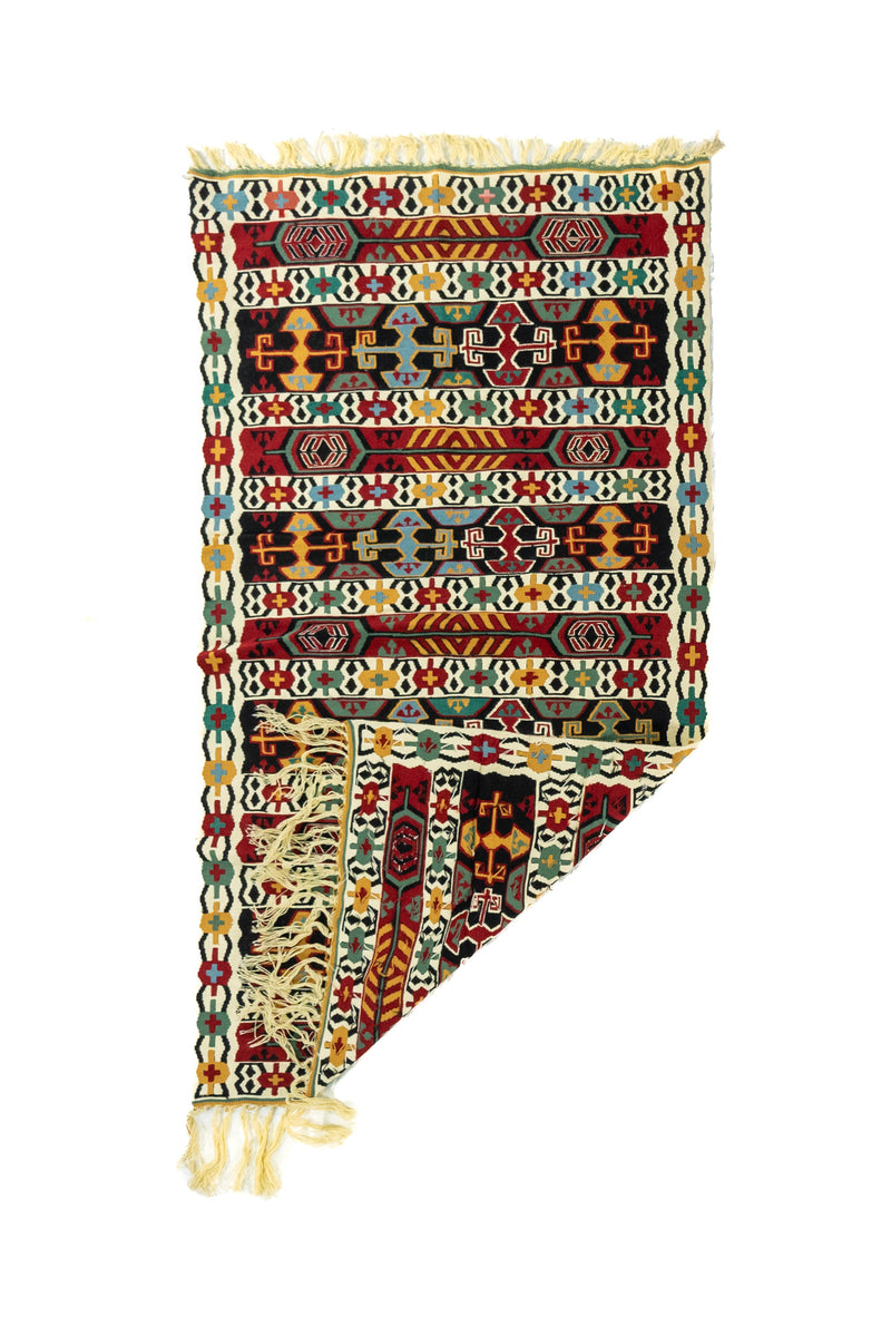 Alfombra tejida a mano con diseño geométrico de franjas horizontales y una esquina doblada que deja ver el reverso y los flecos