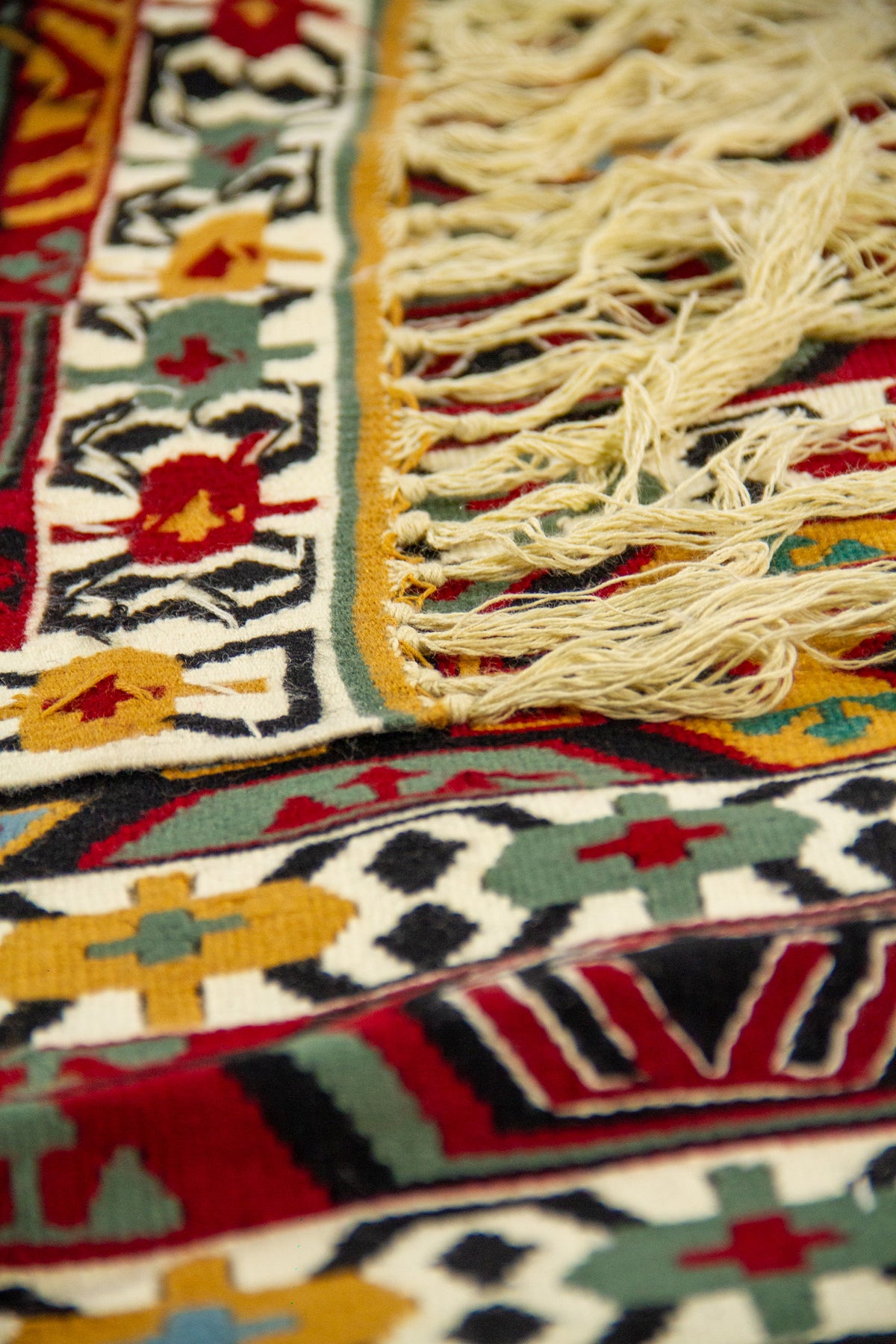 Detalle cercano de alfombra doblada que muestra la textura del tejido, los flecos y los motivos geométricos tradicionales