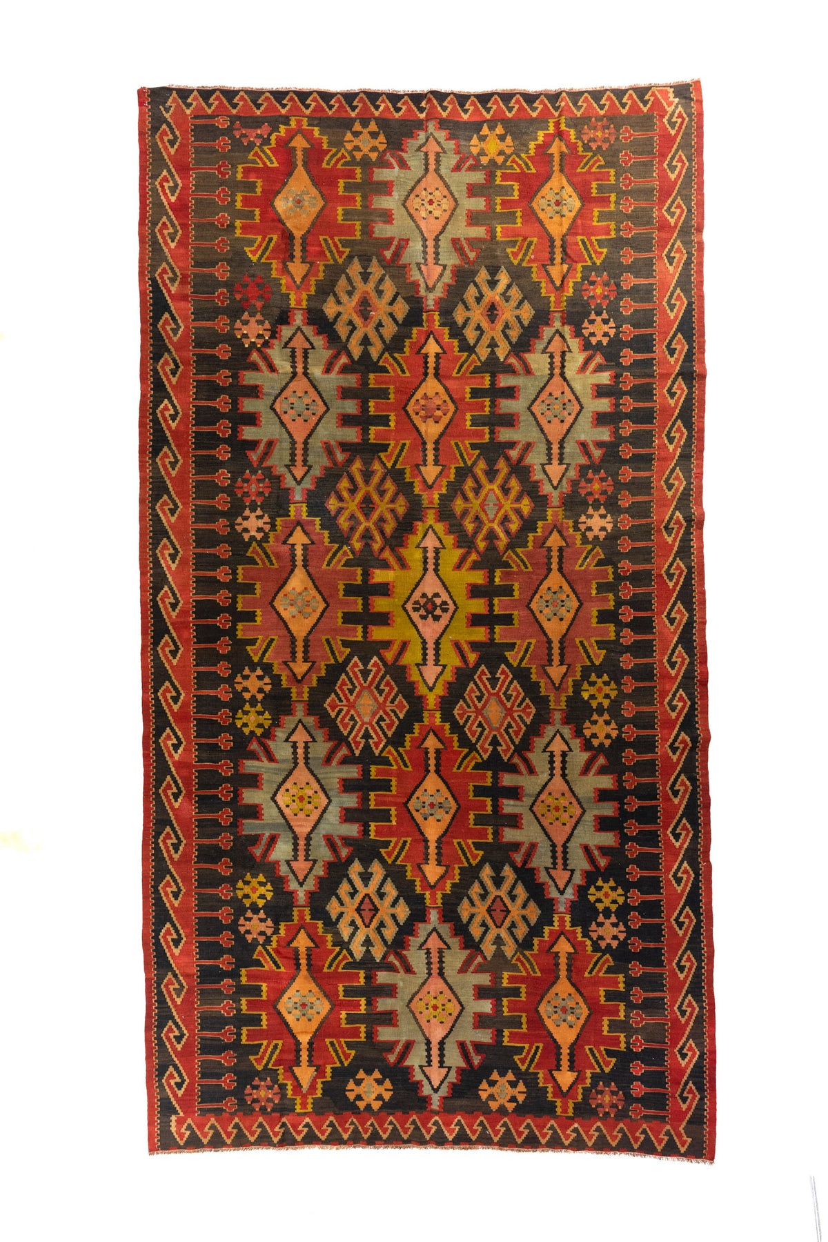 Alfombra de tejido plano con fondo rojo, motivos geométricos en negro, beige y dorado, vista completa.
