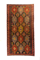 Alfombra de tejido plano con fondo rojo, motivos geométricos en negro, beige y dorado, vista completa.