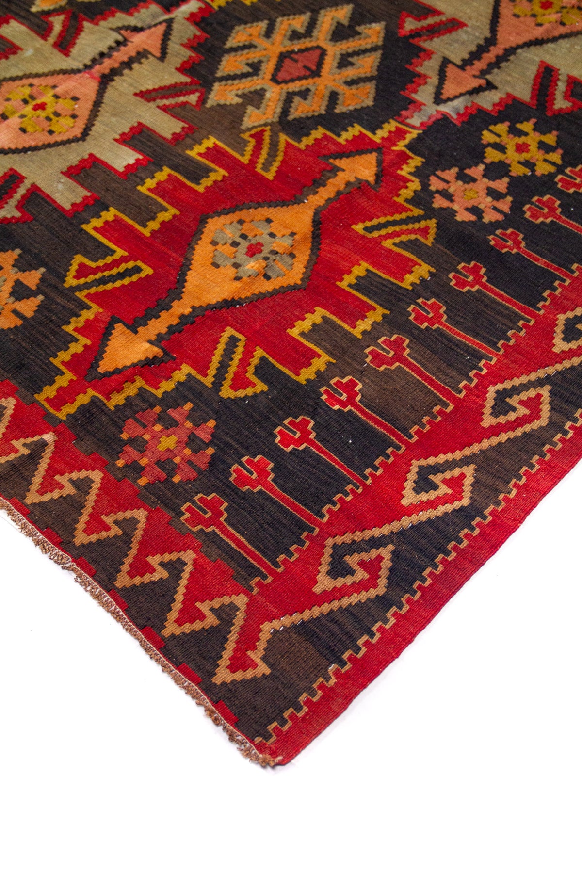 Detalle de esquina de alfombra roja con guarda geométrica y figura central alargada en tonos beige y naranja.