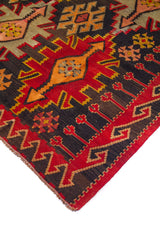 Detalle de esquina de alfombra roja con guarda geométrica y figura central alargada en tonos beige y naranja.