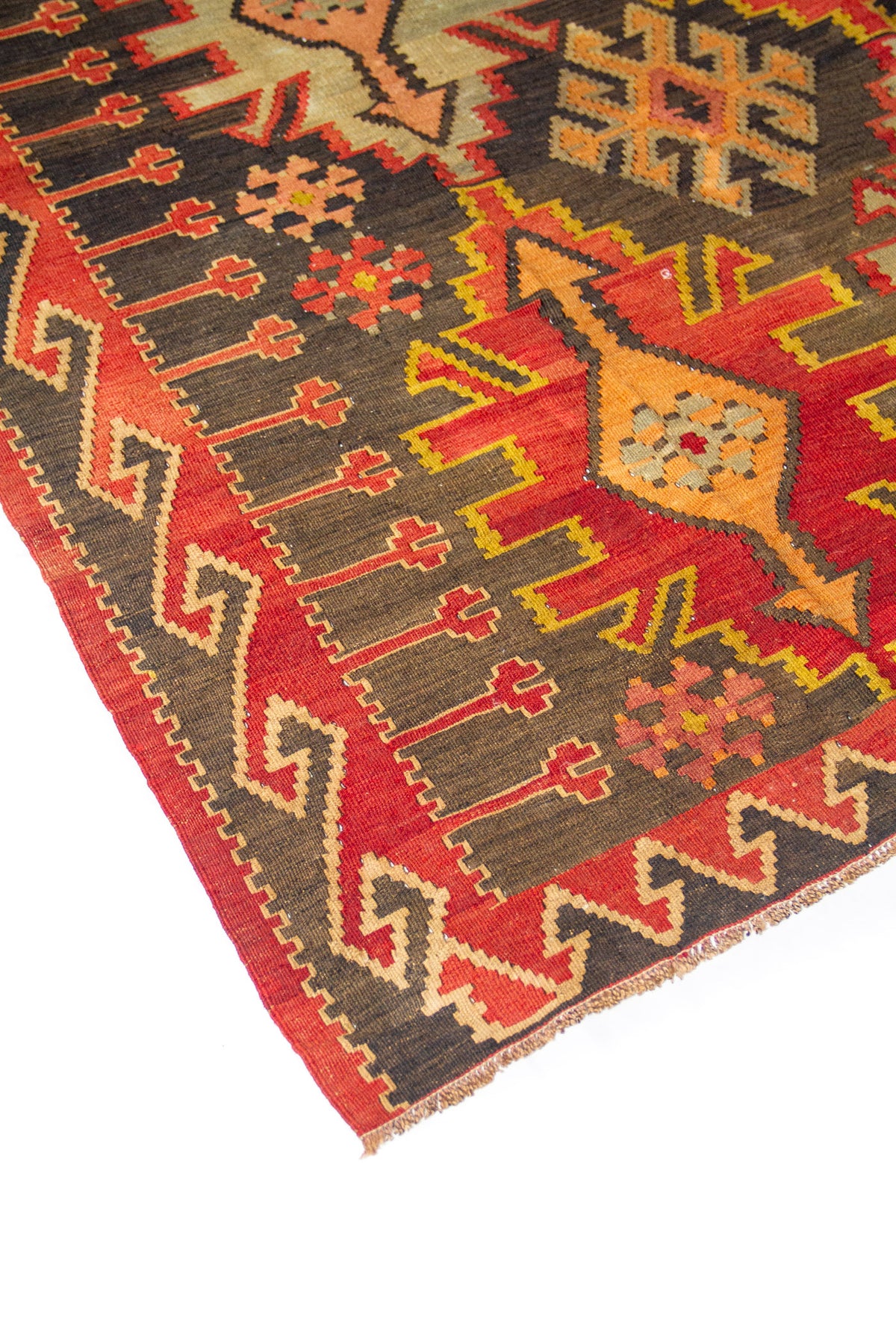 Detalle lateral de alfombra con borde geométrico, pequeños motivos florales y diseño central en tonos rojo y negro.